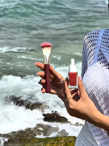 GlowDeer liquid brush and liquid blush held up by the sea